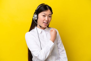 Sarı arka planda izole edilmiş kulaklıkla çalışan pazarlamacı Çinli kadın zaferi kutluyor.