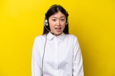 Tele pazarlamacı Çinli kadın, sarı arka planda, şaşırtıcı bir yüz ifadesi olan bir kulaklıkla çalışıyor.