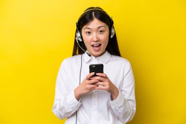 Sarı arka planda izole edilmiş kulaklıkla çalışan pazarlamacı Çinli kadın şaşırdı ve bir mesaj gönderdi.
