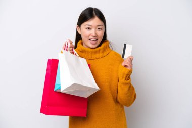 Beyaz arka planda izole edilmiş genç bir Çinli kadın elinde alışveriş çantaları ve bir kredi kartı tutuyor.