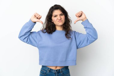 Beyaz arka planda izole edilmiş genç bir Rus kız baş parmağını iki eliyle aşağı gösteriyor.