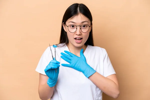 牙医中国女人拿着因米色背景而被隔离的工具 看着右边 感到惊讶和震惊 — 图库照片