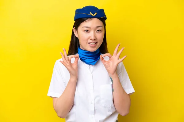 飞机上的中国妇女空姐被隔离在黄色的背景下 手指上显示出一个还好的标志 — 图库照片