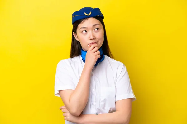Airplane Chinese woman stewardess isolated on yellow background having doubts and with confuse face expression