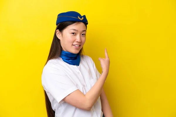 Airplane Chinese woman stewardess isolated on yellow background pointing back