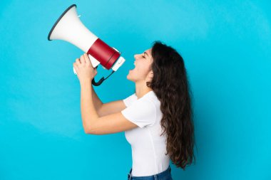 Genç Rus kız, mavi arka planda izole edilmiş bir şekilde megafonla bir şey duyurmak için bağırıyor.