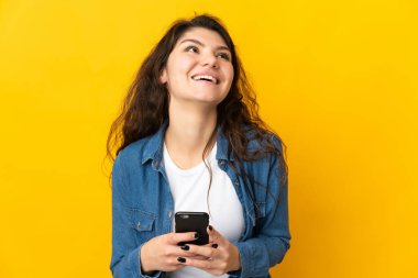 Genç Rus kız, sarı arka planda cep telefonu kullanarak izole edilmiş.