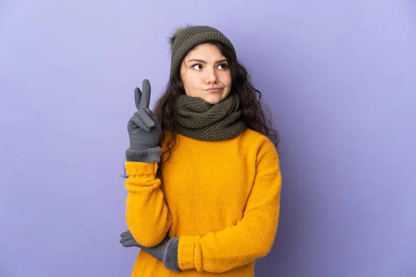 俄罗斯少女 头戴冬季帽子 背景为紫色 手指头交叉 祝愿好运 — 图库照片