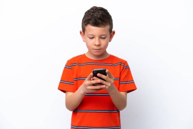 Beyaz arka planda izole edilmiş küçük çocuk cep telefonuyla bir mesaj gönderiyor.