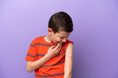 Yara bandı takan küçük çocuk, mor arka planda, şaşırmış ve şok olmuş bir yüz ifadesiyle izole edilmiş.