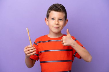 Küçük çocuk mor arka planda dişlerini fırçalıyor. Başparmakları havada. Çünkü iyi bir şey oldu.