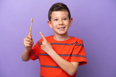 Küçük bir çocuk mor arka planda izole edilmiş dişlerini fırçalıyor ve onu işaret ediyor.