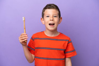 Mor arka planda diş fırçalayan küçük çocuk şaşırmış ve şok olmuş bir yüz ifadesiyle.