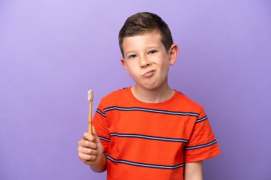 Dişlerini fırçalayan küçük çocuk mor arka planda üzgün bir ifadeyle izole edilmiş.