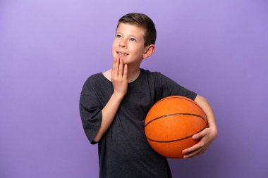 Mor arka planda izole edilmiş basketbol oynayan küçük çocuk gülümserken yukarı bakıyor.
