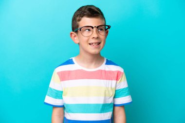 Küçük çocuk mavi arka planda gözlüklü ve düşünürken yukarı bakıyor.