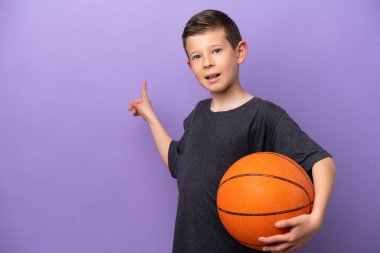 Mor arka planda izole edilmiş basketbol oynayan küçük çocuk geriye işaret ediyor