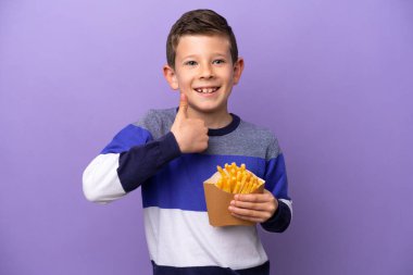 Mor arka planda izole edilmiş patates kızartması tutan küçük bir çocuk baş parmak hareketi yapıyor.