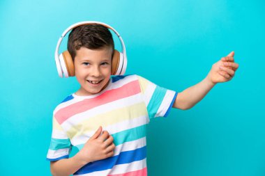 Küçük çocuk mavi arka planda müzik dinleyip gitar hareketi yapıyor.