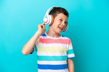 Küçük çocuk mavi arka planda izole edilmiş müzik dinliyor ve şarkı söylüyor.