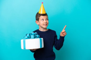 Mavi arka planda izole edilmiş doğum günü pastası tutan küçük çocuk harika bir fikre işaret ediyor.