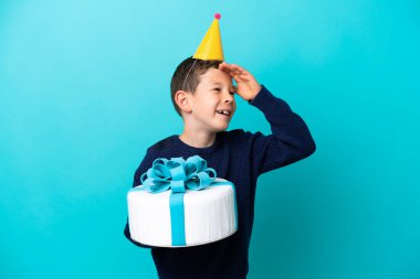 Mavi arka planda izole edilmiş doğum günü pastası tutan küçük çocuk çok gülümsüyor.