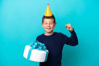 Küçük çocuk elinde pastayla mavi arka planda izole bir şekilde güçlü bir jest yapıyor.