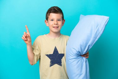 Mavi arka planda izole edilmiş pijamalı küçük çocuk harika bir fikre işaret ediyor.