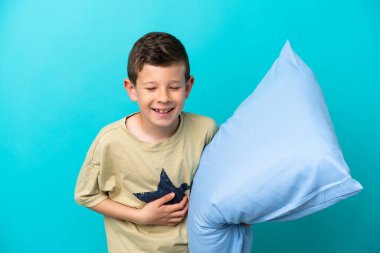 Mavi arka planda izole edilmiş pijamalı küçük bir çocuk çok gülümsüyor.