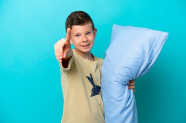 Mavi arka planda izole edilmiş pijamalı küçük çocuk parmağını kaldırıyor ve gösteriyor.
