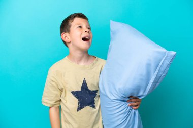 Pijamalı küçük çocuk mavi arka planda yalnız gülüyor.