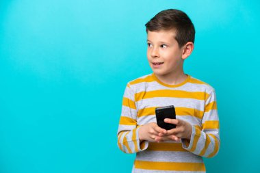 Küçük çocuk mavi arka planda cep telefonuyla izole edilmiş.
