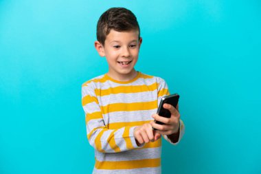 Küçük çocuk mavi arkaplanda izole edilmiş. Cep telefonuyla bir mesaj ya da e-posta gönderiyor.