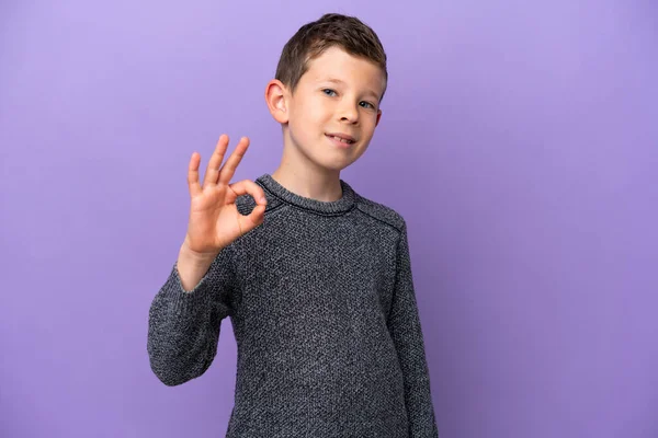 在紫色背景上被隔离的小男孩用手指表现出了好的体征 — 图库照片