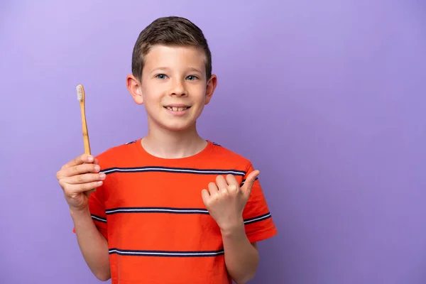 製品を提示するために側面を指す紫色の背景に隔離された小さな男の子のブラッシング歯 — ストック写真