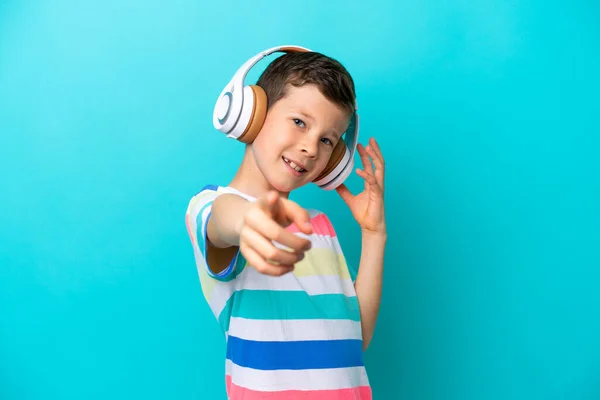 小男孩被蓝色背景隔离 一边听着音乐 一边指着前面 — 图库照片