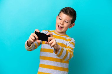 Küçük çocuk mavi arka planda izole edilmiş cep telefonuyla oynuyor.