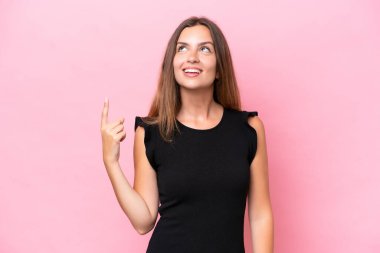 Pembe arka planda izole edilmiş genç beyaz kadın yukarı bakıyor ve şaşırıyor.