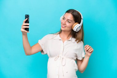 Kafkasyalı genç bir kadın mavi arka planda izole edilmiş hamile ve selfie çekiyor.