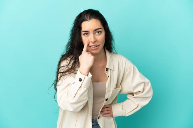 Mavi arka planda izole edilmiş genç beyaz kadın bir şey gösteriyor.