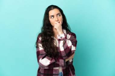 Kafkasyalı genç bir kadın mavi arka planda izole edilmiş. Şüpheleri var ve kafası karışmış bir yüz ifadesi var.