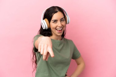 Pembe arka planda izole edilmiş beyaz bir kadın müzik dinliyor.