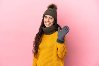 Mor arka planda izole edilmiş, elinde mutlu bir ifadeyle selam veren, kışlık şapkalı beyaz bir kız.