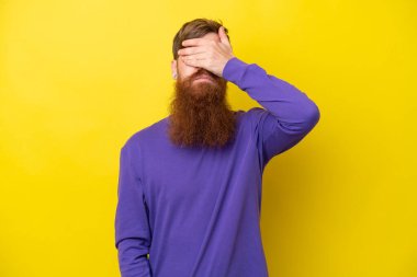 Sakallı kızıl saçlı adam sarı arka planda tek başına gözlerini elleriyle kapatıyor. Bir şey görmek istemiyorum.