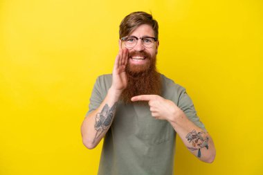 Sarı arka planda sakallı kızıl saçlı bir adam bir ürün sunmak ve bir şeyler fısıldamak için kenarı işaret ediyor.