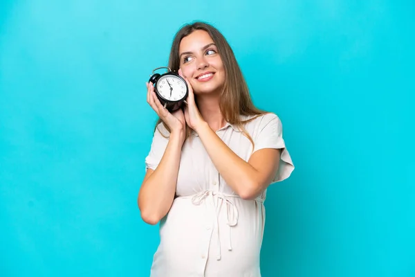 Young Caucasian Woman Isolated Blue Background Pregnant Holding Clock — Fotografia de Stock