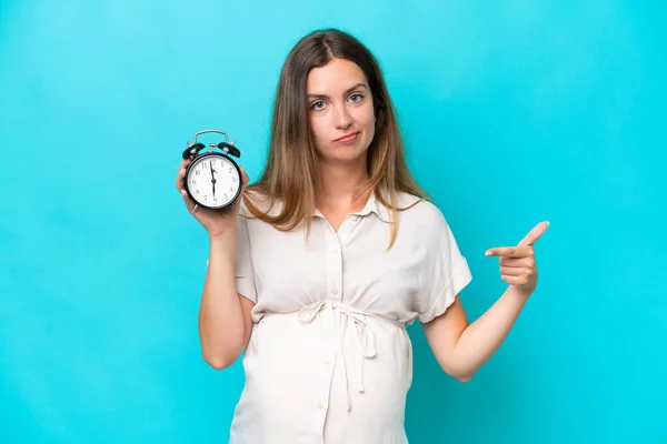 Young Caucasian Woman Isolated Blue Background Pregnant Holding Clock Stressed — Φωτογραφία Αρχείου