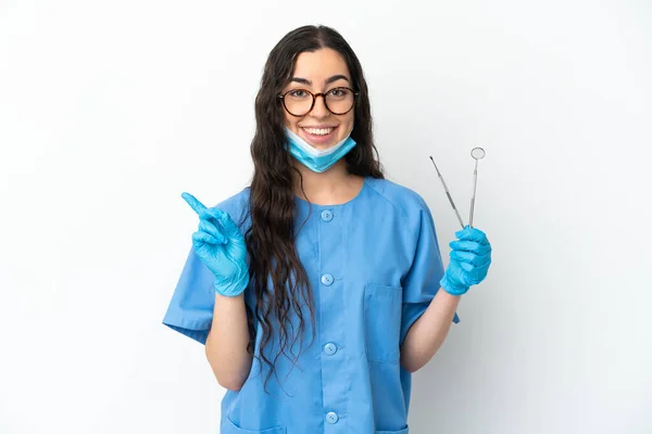 年轻的女牙医拿着被白色背景隔离的工具 指向侧面来展示一种产品 — 图库照片