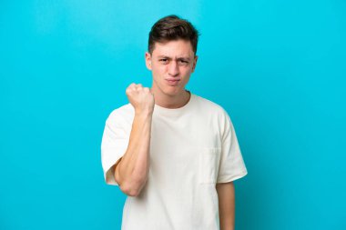 Genç yakışıklı Brezilyalı adam mutsuz bir ifadeyle mavi arka planda izole edilmiş.