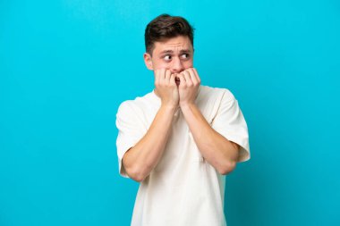 Genç ve yakışıklı Brezilyalı bir adam mavi arka planda izole edilmiş gergin ve korkmuş bir şekilde elleriyle suni teneffüs yapıyor.